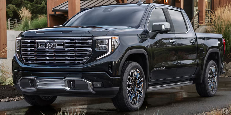 Black GMC Sierra Denali pickup truck parked in a driveway in front of a house.