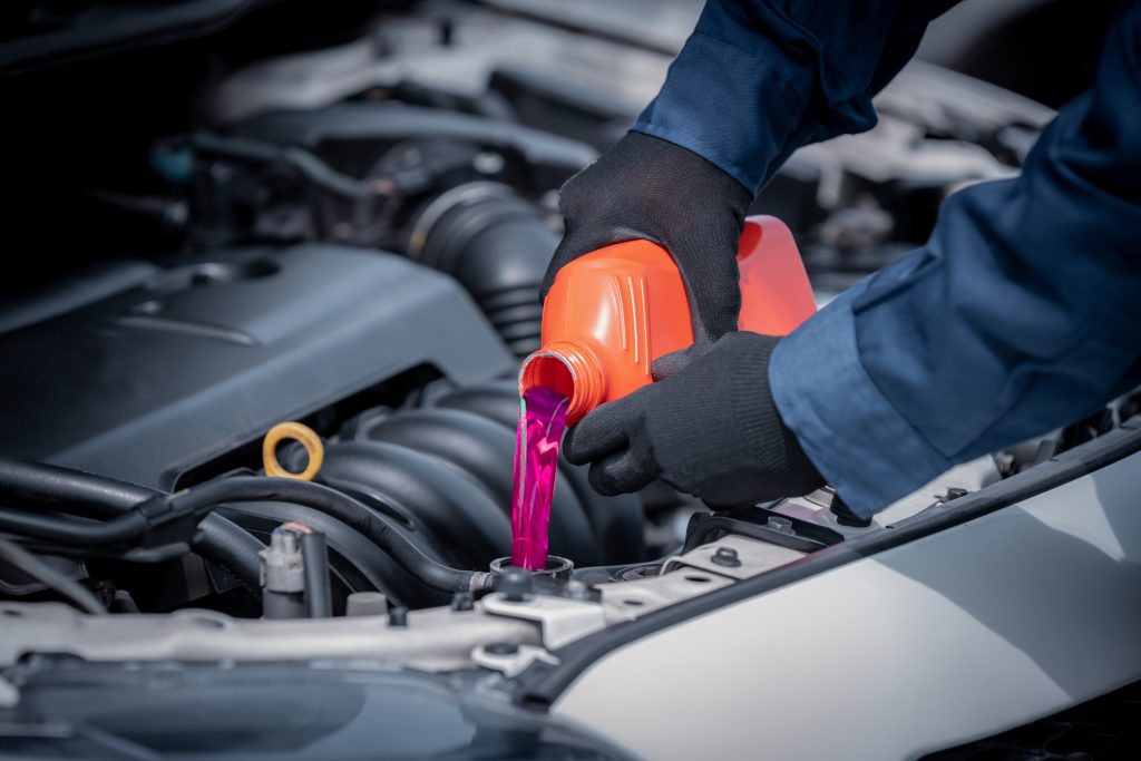 Mechanic pouring pink coolant into a car engine reservoir.