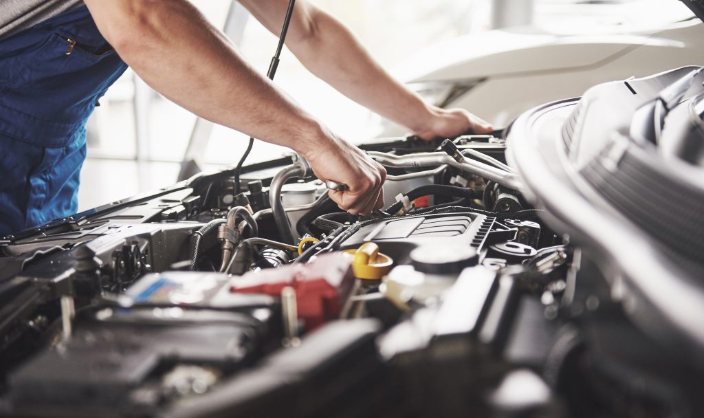 Automotive technician inspecting a vehicle engine during maintenance service.