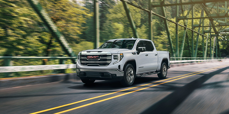 White GMC Sierra 1500 pickup truck driving on a scenic road.