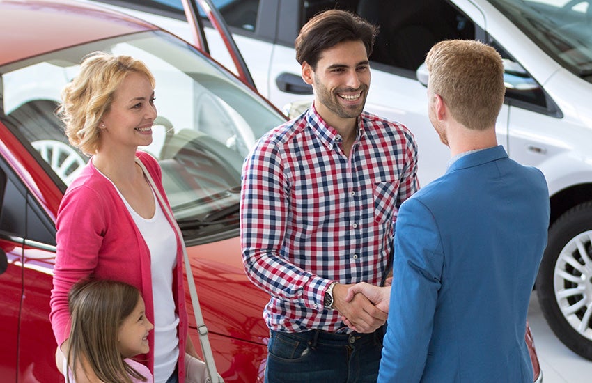 Una familia sonriente estrecha la mano de un vendedor de coches en un concesionario.