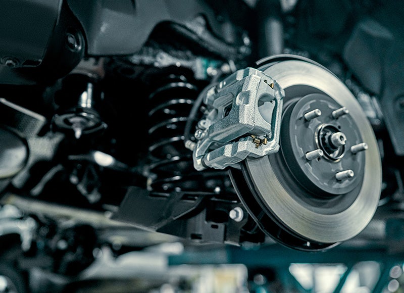 Close-up of a car brake rotor and caliper under a vehicle in a service bay.
